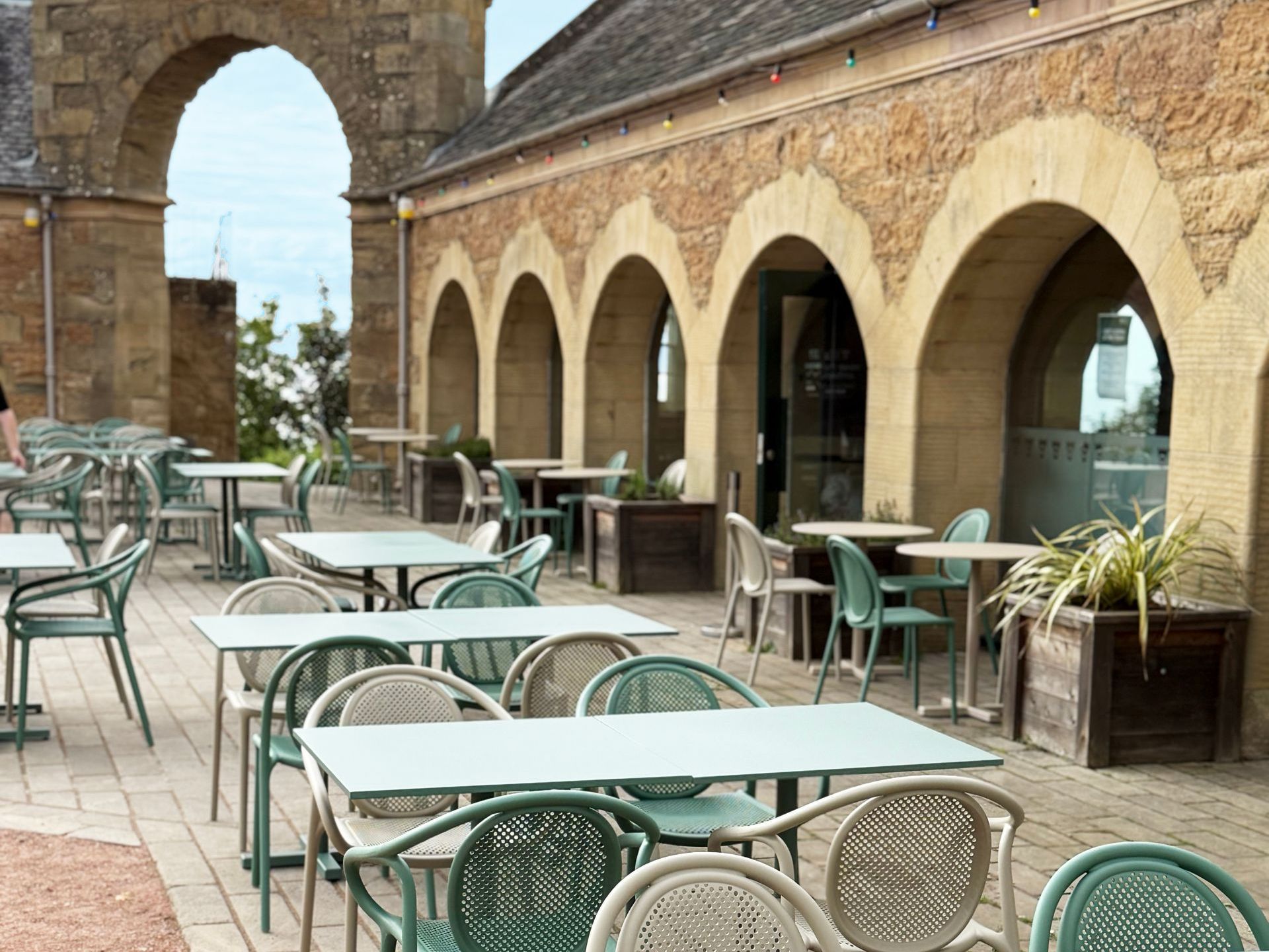 Culzean castle outdoor cafe are with tables and chairs under arched stone structure.