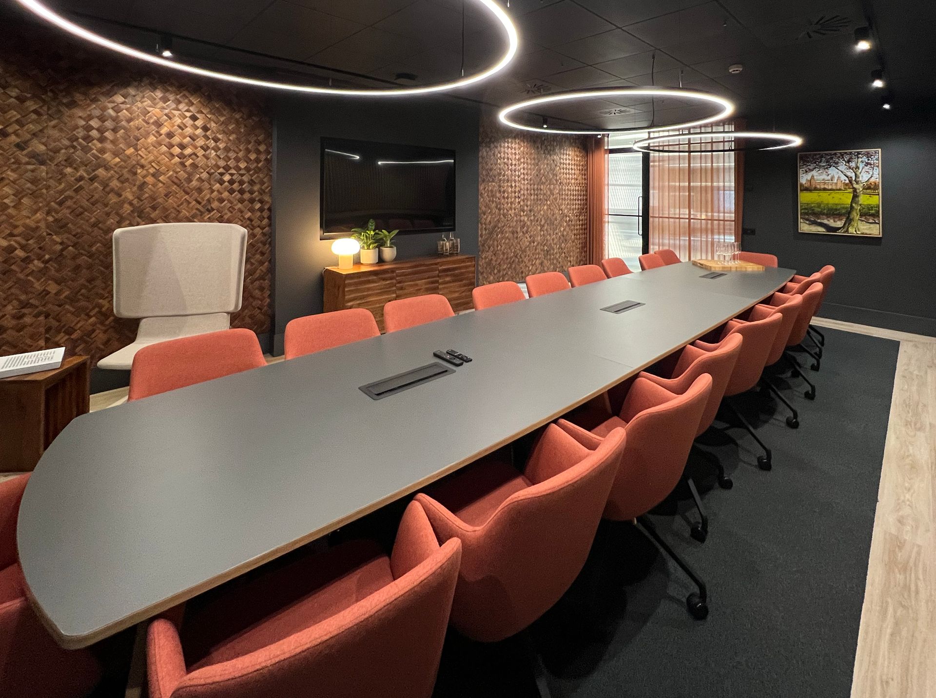 Conference room with long table, orange chairs, and wood-paneled wall.