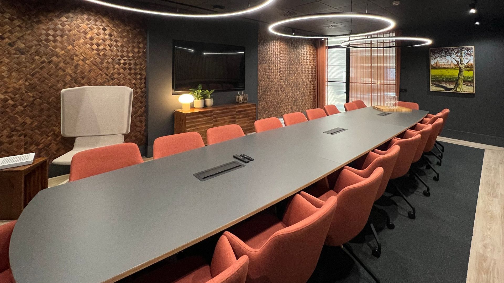 A long conference table with red chairs in a modern office. Textured wall and art visible.