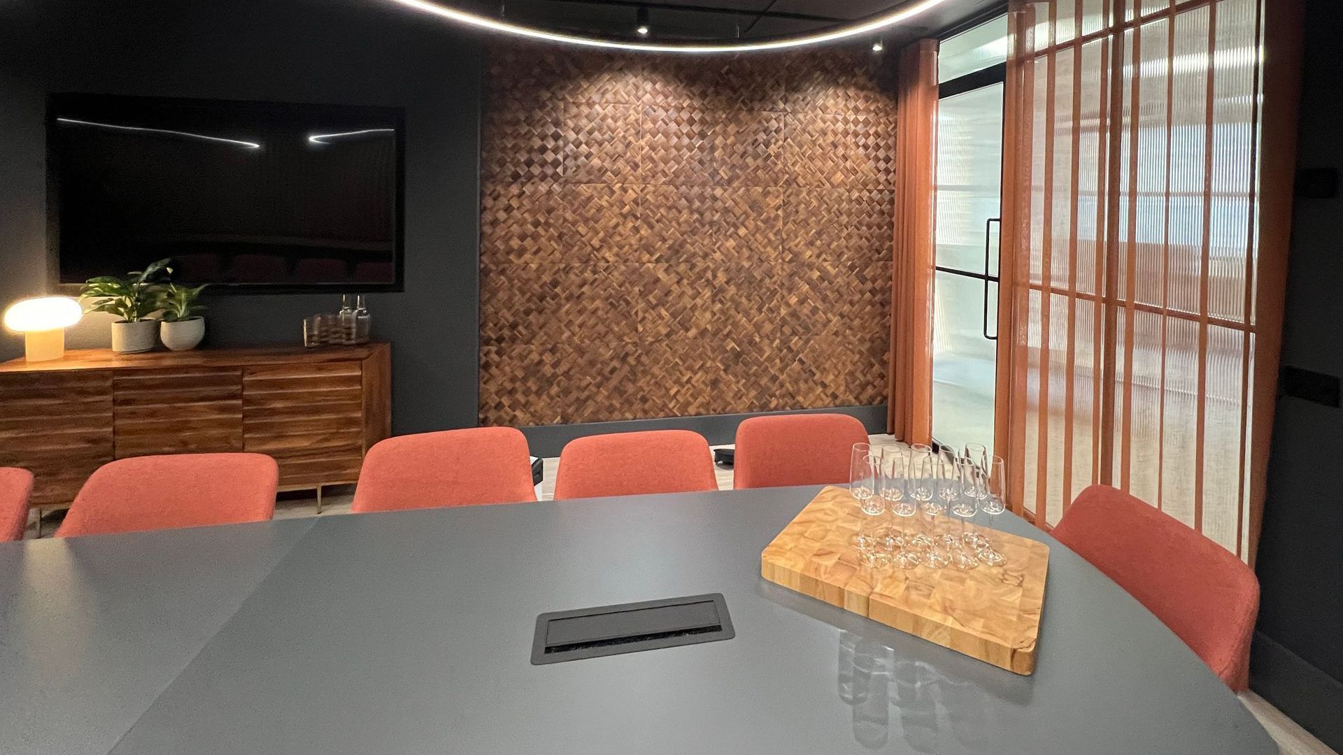 Conference room with large table, coral chairs, wood accent wall, and modern lighting.