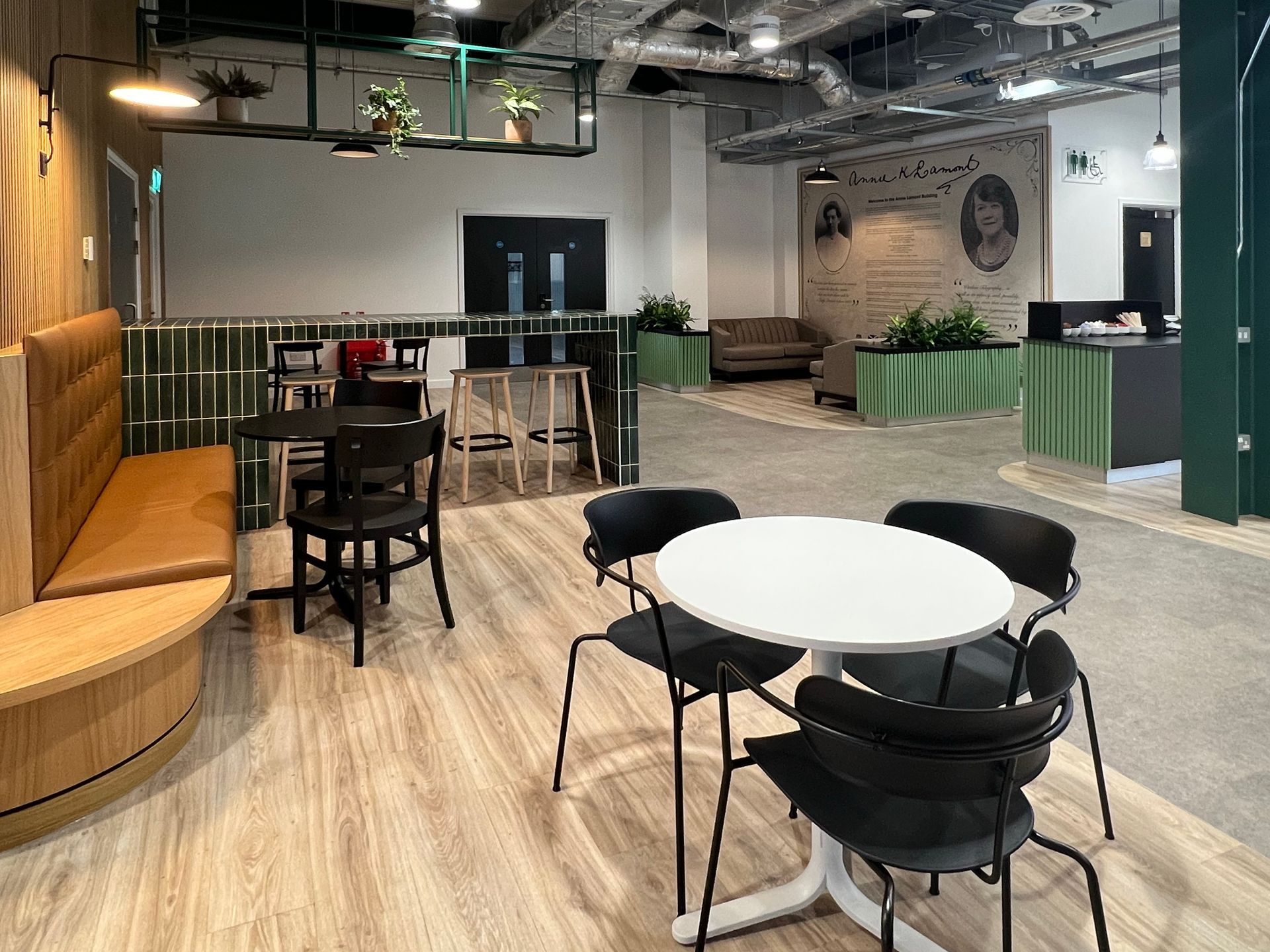 The photo captures the ecclectic mixture of colours and textures in Annie's Cafe, focusing on a white circular table with black dining chairs, a leather bench seating, a dark-green tiled counter with wooden stools, and in the background, some low sofas against a large mural.