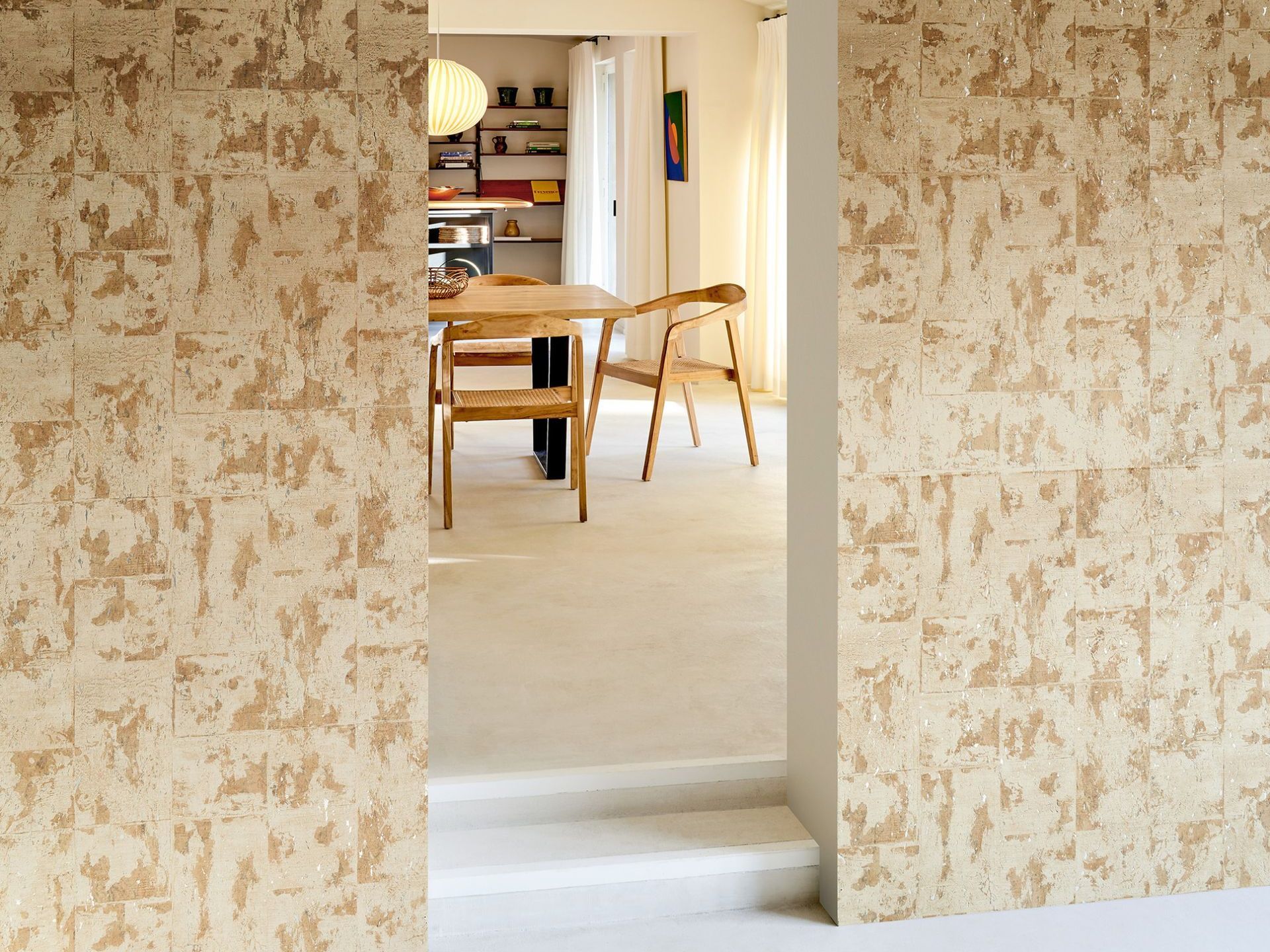 Wall with textured beige panels, doorway into a dining area with wooden furniture.