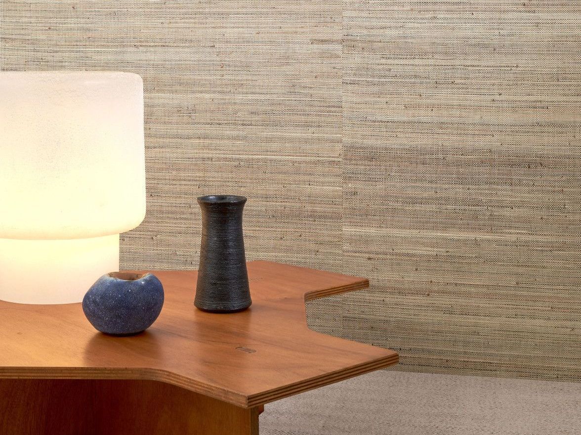 A wooden table with a lamp, blue apple, and vase in front of a textured wall.