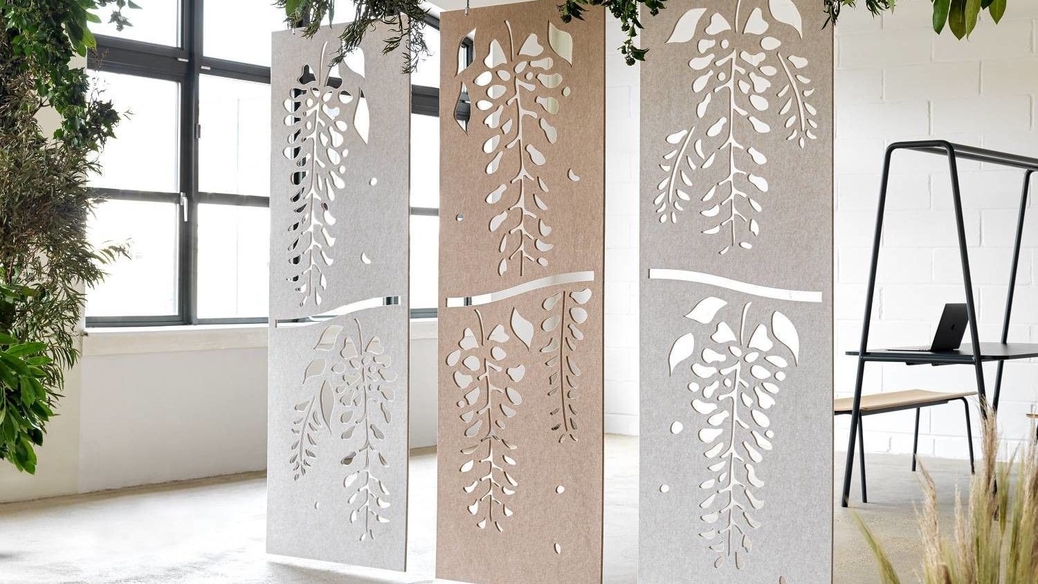 the photo highglghts three room dividers made of gray and beige materials. there is a stenciled cut out of leaves on the dividers to bring in biophilic design. 