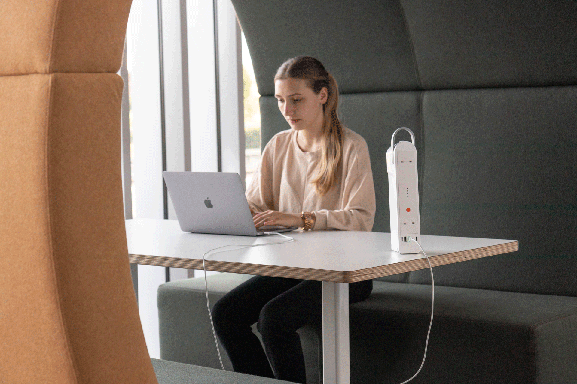 Woman in office booth using a laptop, with a white device on the table.