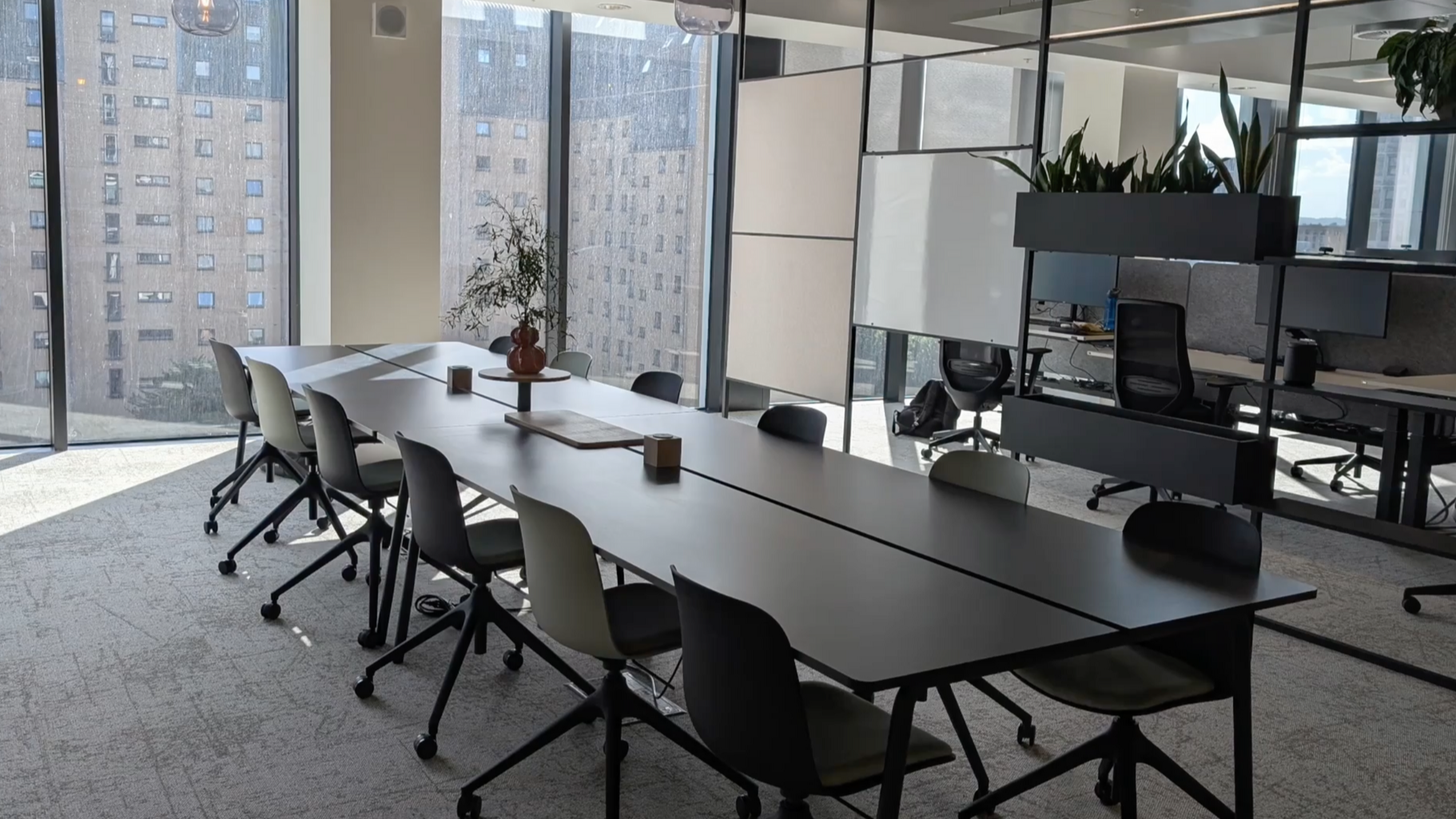 A long, black conference table with chairs in an office setting near a window.