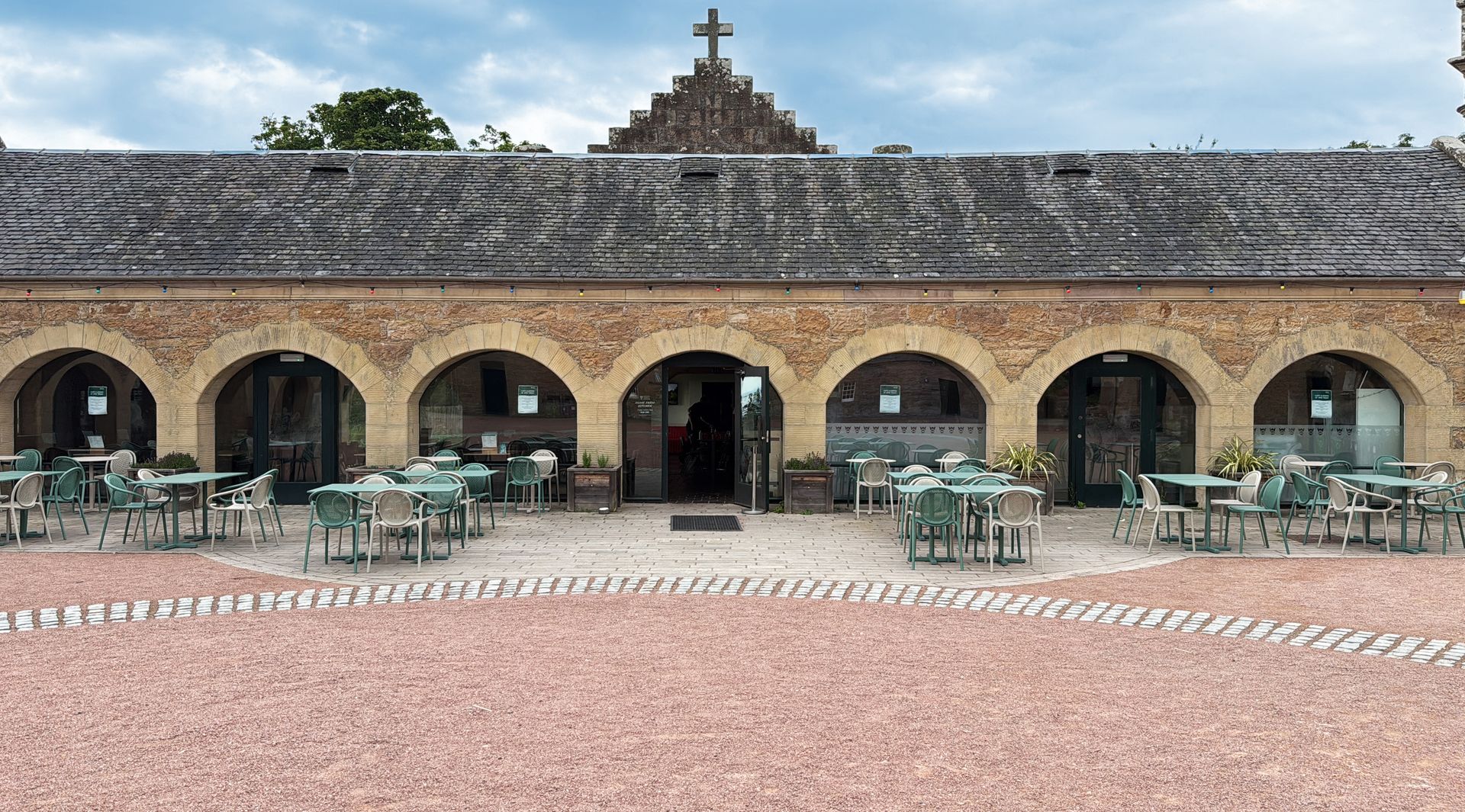 Exterior of a restaurant with arched openings, outdoor seating, and a cross atop the building.