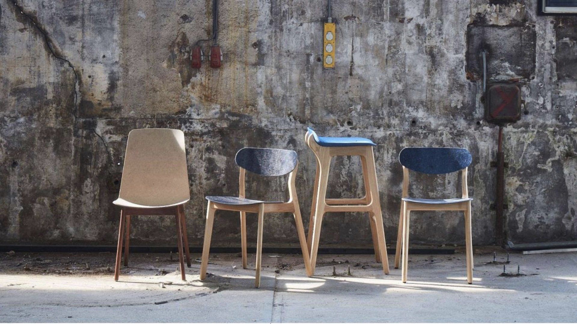 Four modern chairs and a tall stool against a weathered concrete wall.