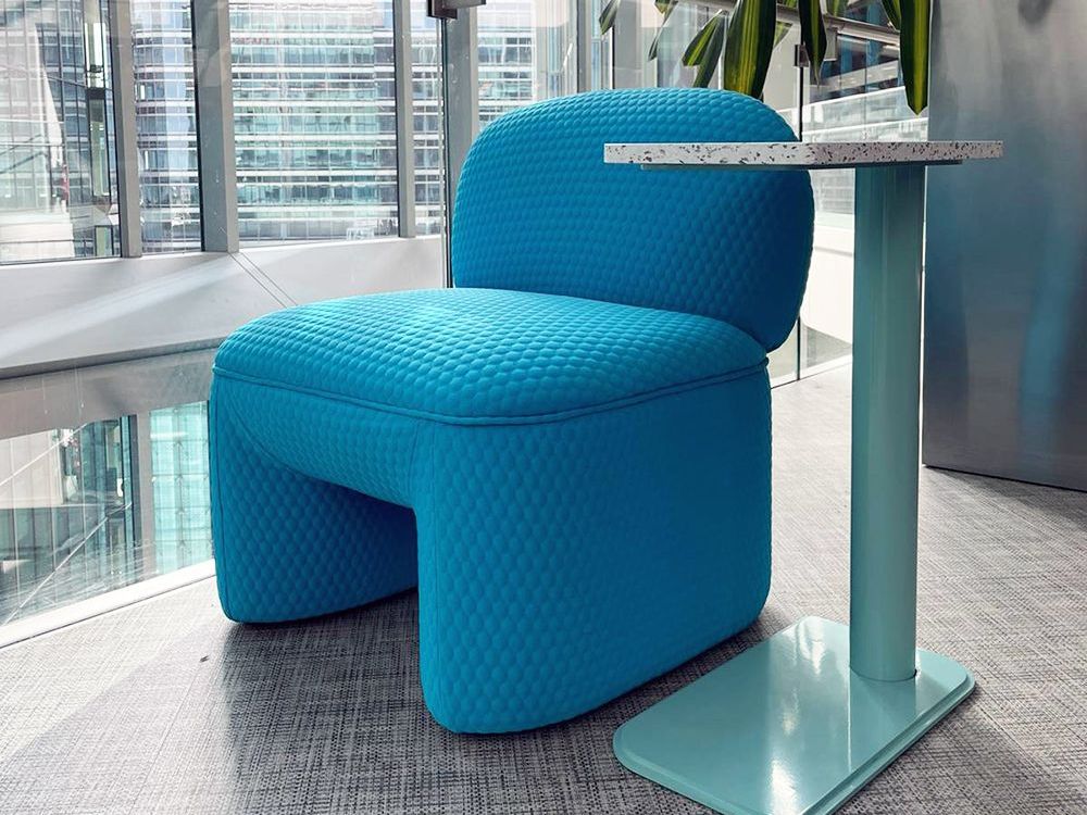 Sustainable furniture blue chair and side table in a brightly lit office setting with a city view.