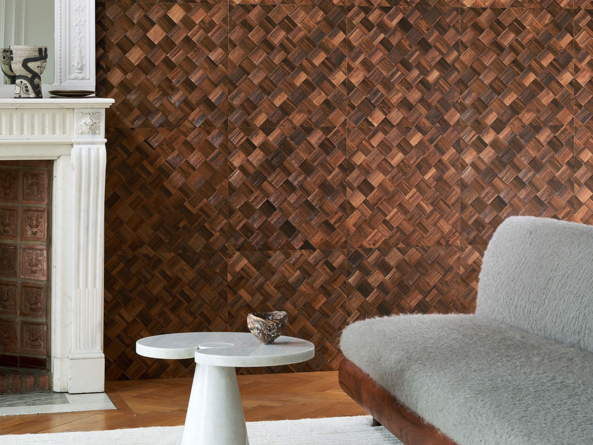 Living room with a brown sustainable banana leaf woven wall, fireplace, gray couch, and white table.