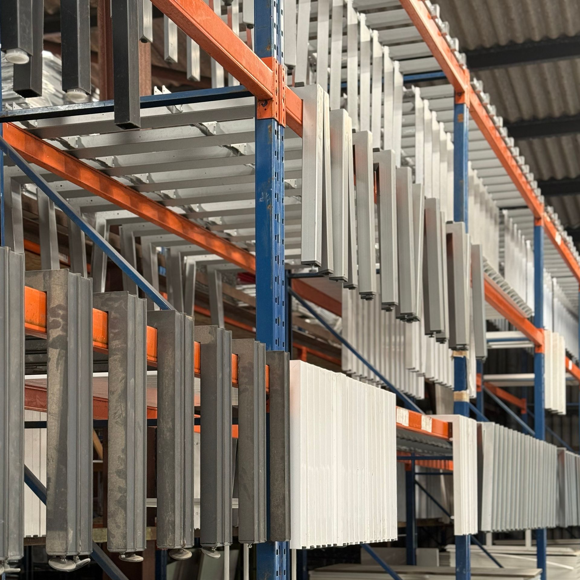 Refurbished metal desk legs hanging on racks in a warehouse in Scotland; some painted white and some in various shades of gray.