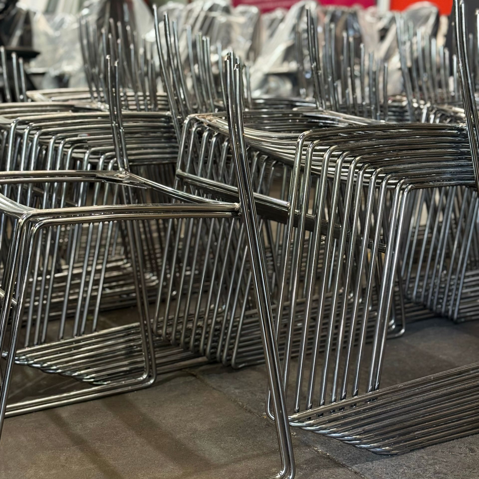 A stack of refurbished second hand metal chair frames in a warehouse. Shiny, chrome-like finish.