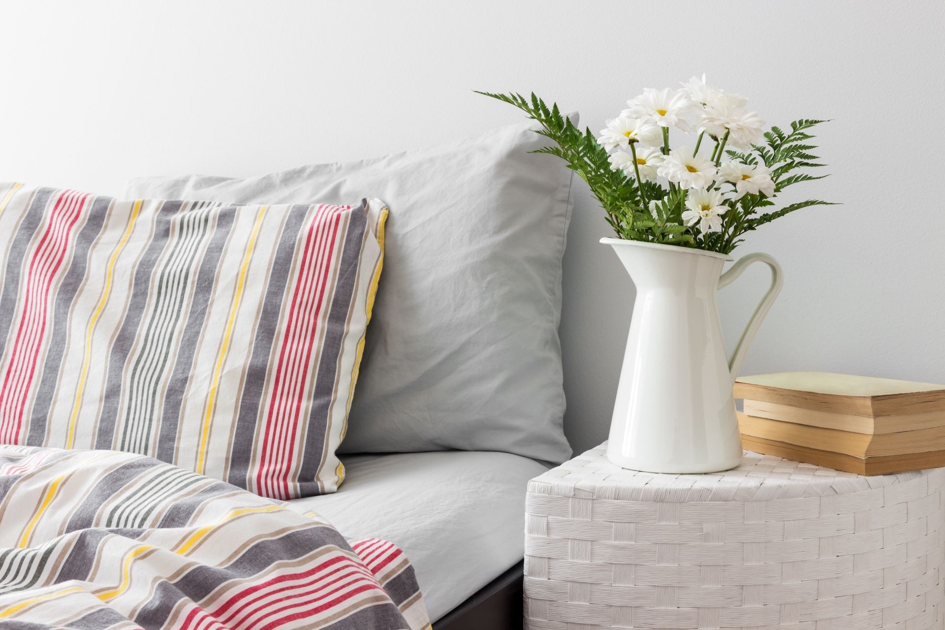 There is a vase of flowers on the nightstand next to the bed.