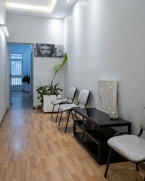 Sala de espera moderna con sillas blancas, una planta en maceta, una mesa negra y suelo de madera.