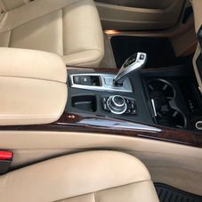 A close-up of a luxury car's center console featuring a gear shifter, iDrive controller, and beige leather interior.