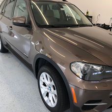 A metallic bronze BMW X5 SUV parked on a white floor inside a bright garage.