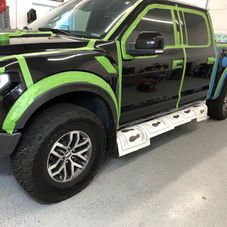 A black pickup truck in a shop, prepped for work with green masking tape on the body panels and paper on the steps.