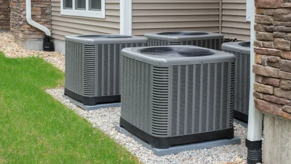 A row of air conditioners are sitting outside of a house.
