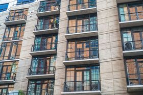 Modern apartment building facade with brick and beige panels, balconies, and large windows