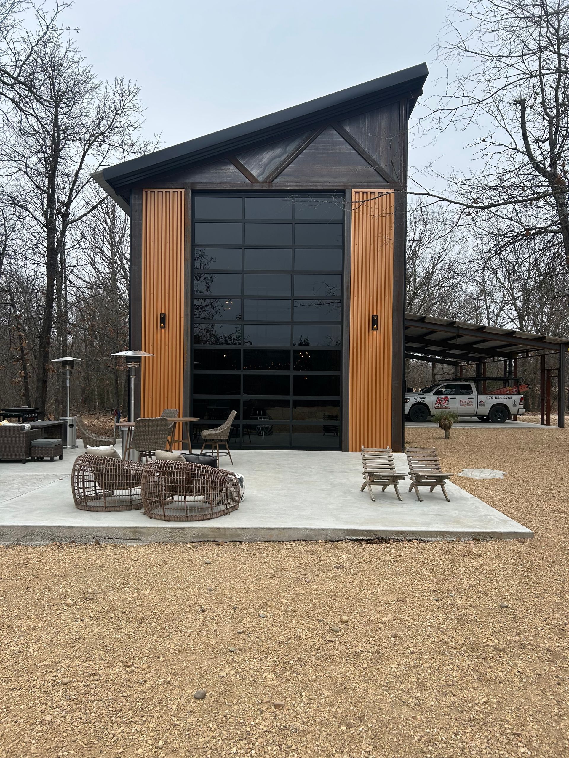 A modern tiny house with a glass garage door, wooden accents, and a concrete patio in a wooded setting.