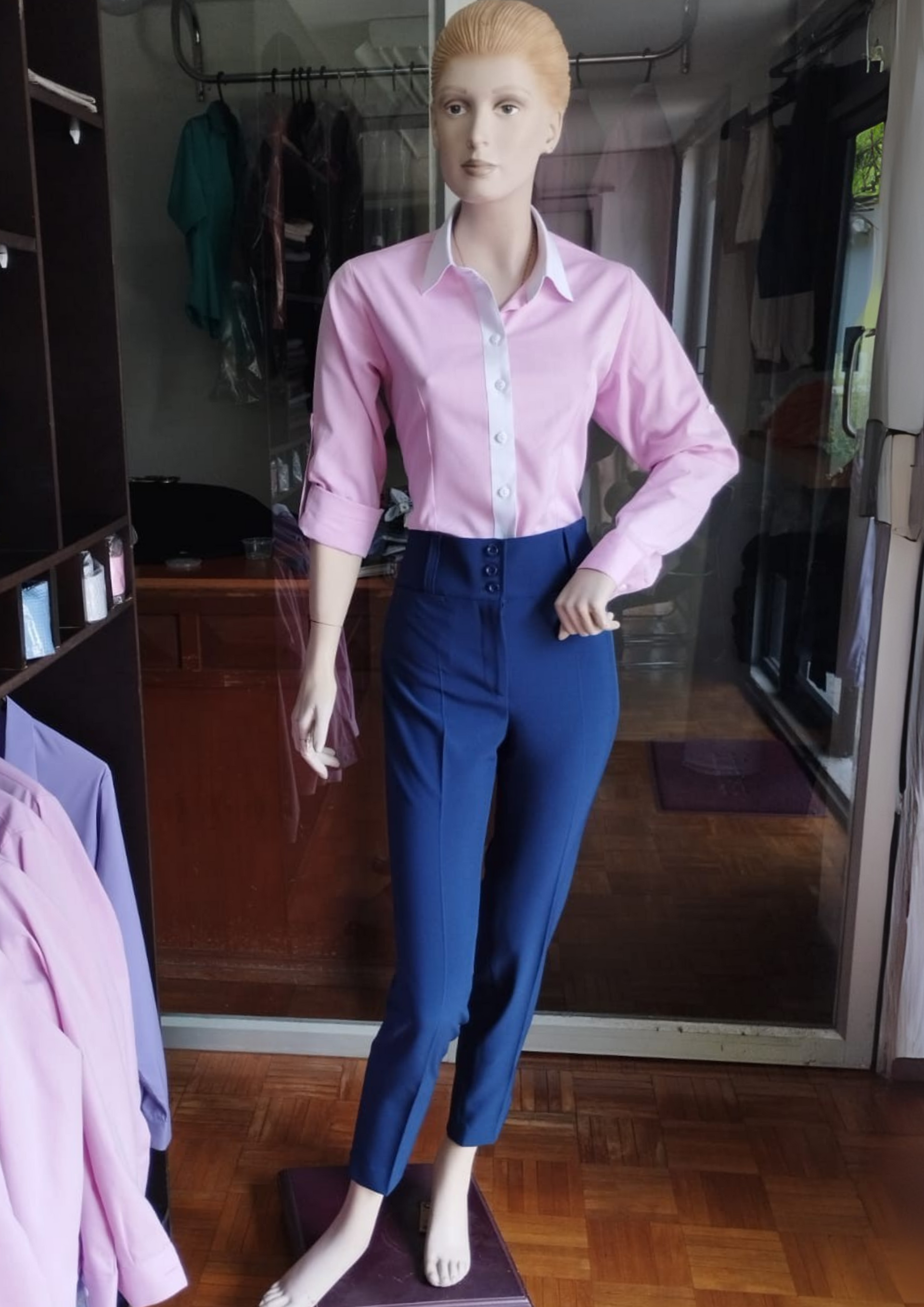 Maniquí con blusa rosa y pantalón azul, de pie en una habitación con percheros y suelos de madera.