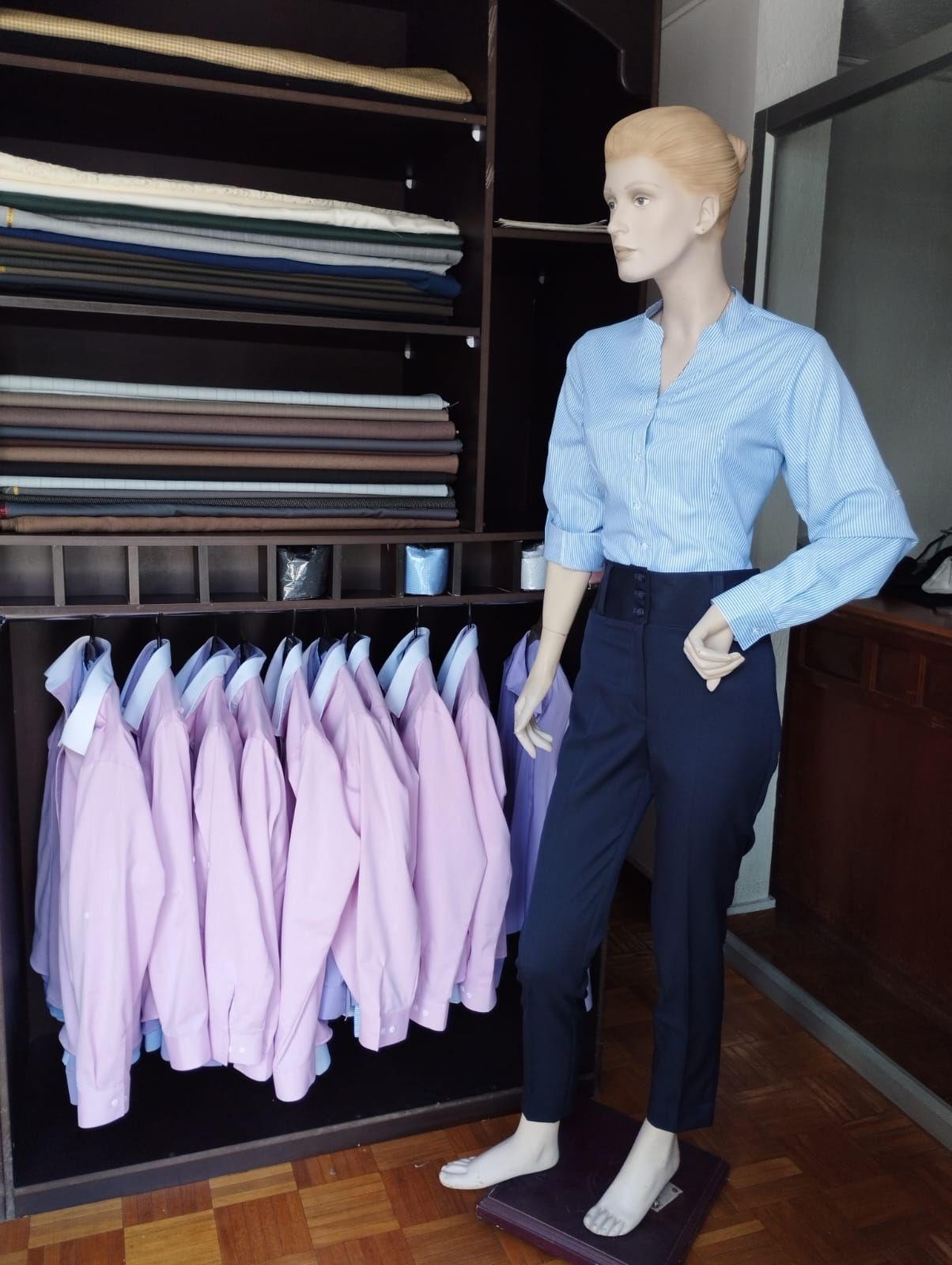Maniquí vestido de azul y negro se encuentra cerca de camisas en un armario, con muestras de tela encima.