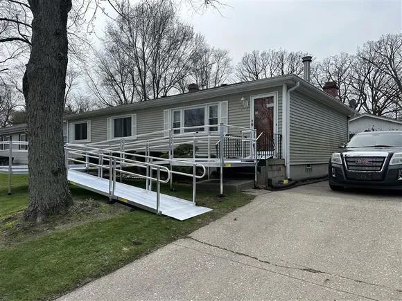 Single-story beige house with wheelchair ramp, parked SUV, and driveway on a cloudy day