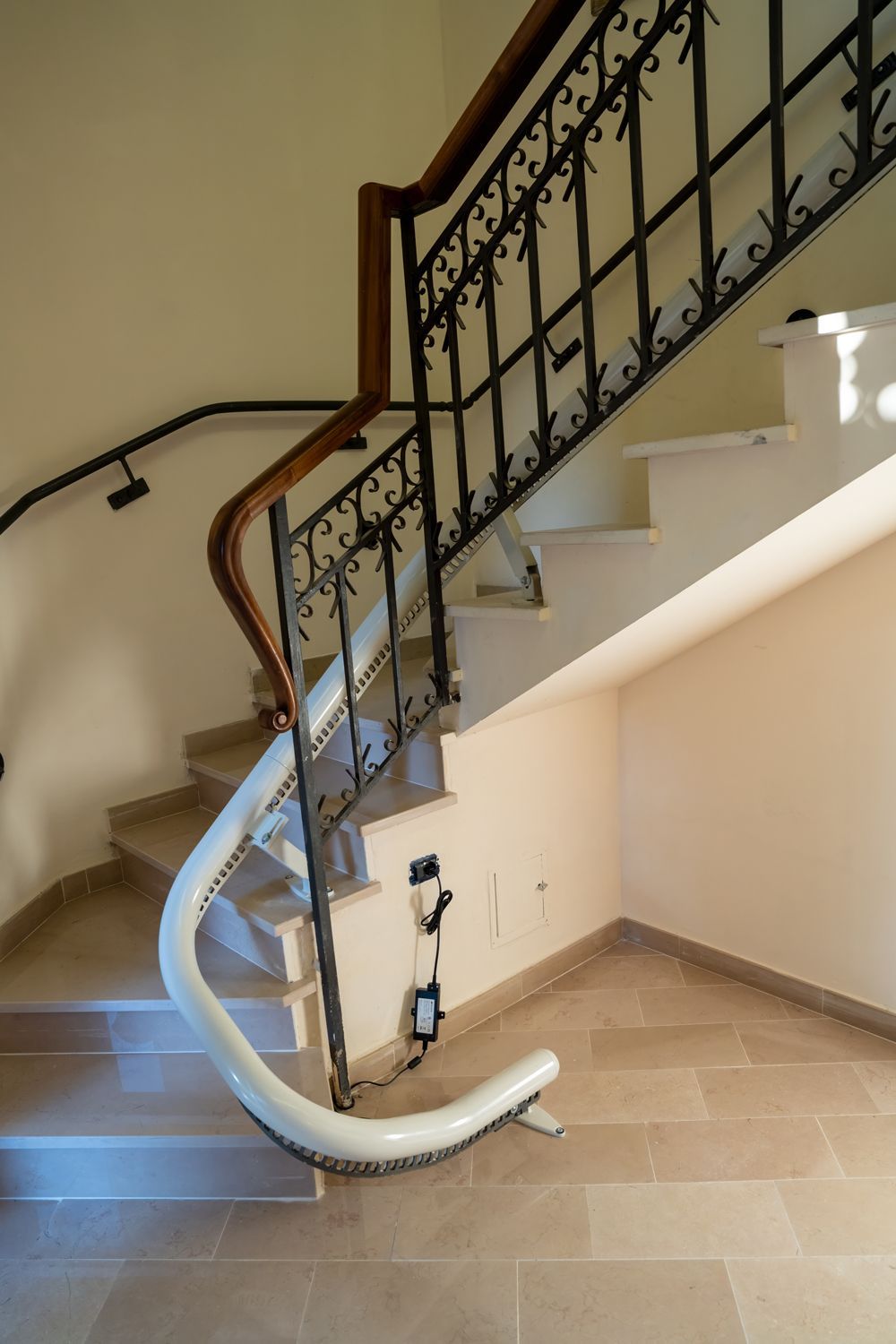 Curved stairlift installed on an indoor staircase with beige steps and black wrought-iron railing.