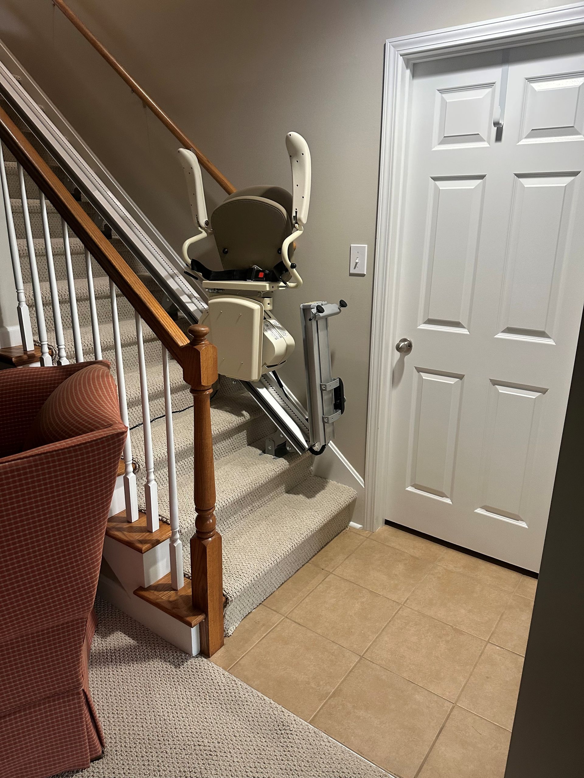Stairlift on a carpeted staircase beside a white front door in a home hallway.