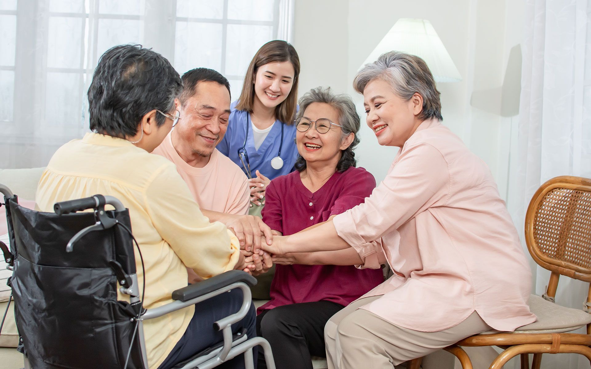 A group of elderly people are sitting around a table holding hands.