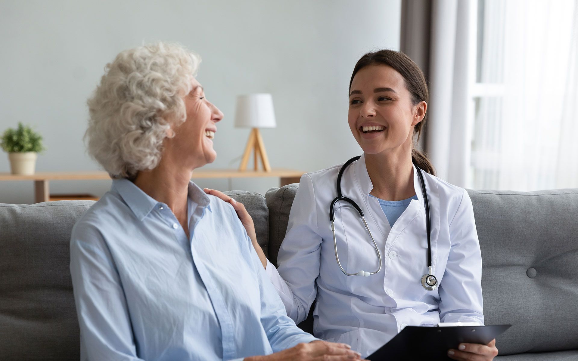 A doctor is talking to an elderly woman while sitting on a couch.