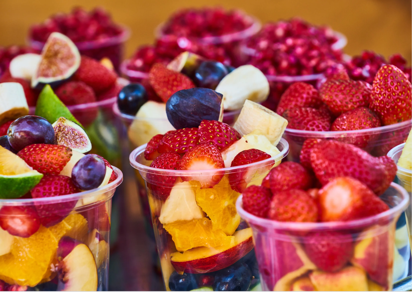 A variety of fruits are in plastic cups on a table.