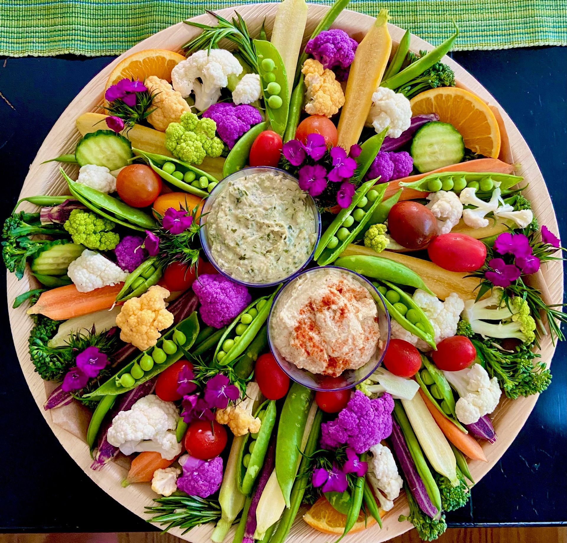 A wooden plate topped with a variety of vegetables and dips.