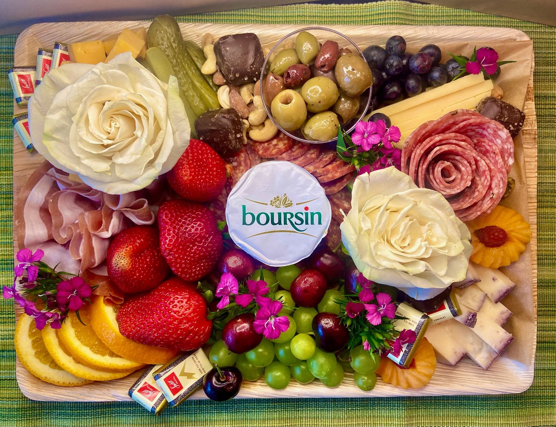 A wooden tray filled with fruit , cheese , nuts , and flowers.