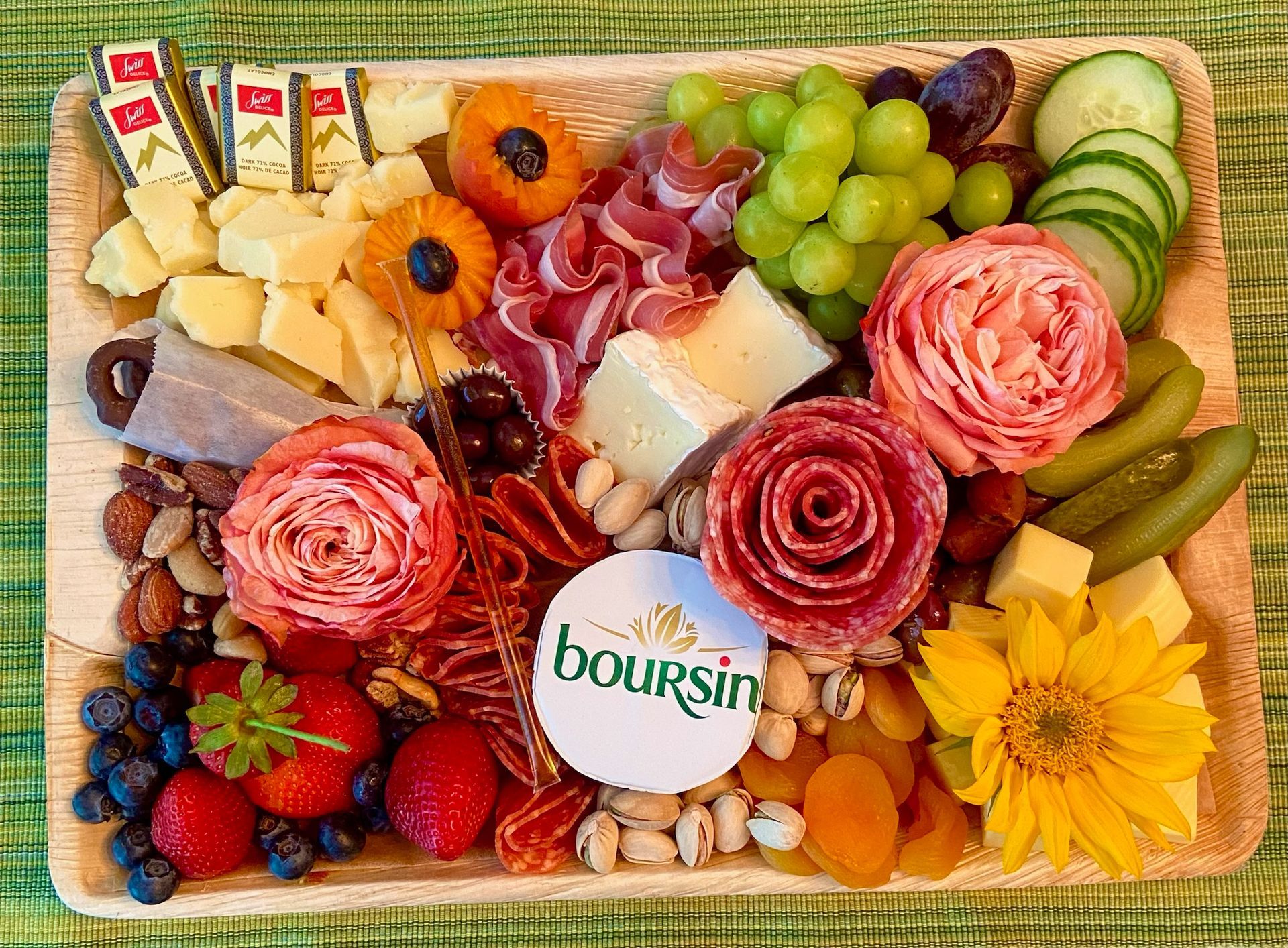 A wooden cutting board filled with fruits , meats , nuts and flowers.