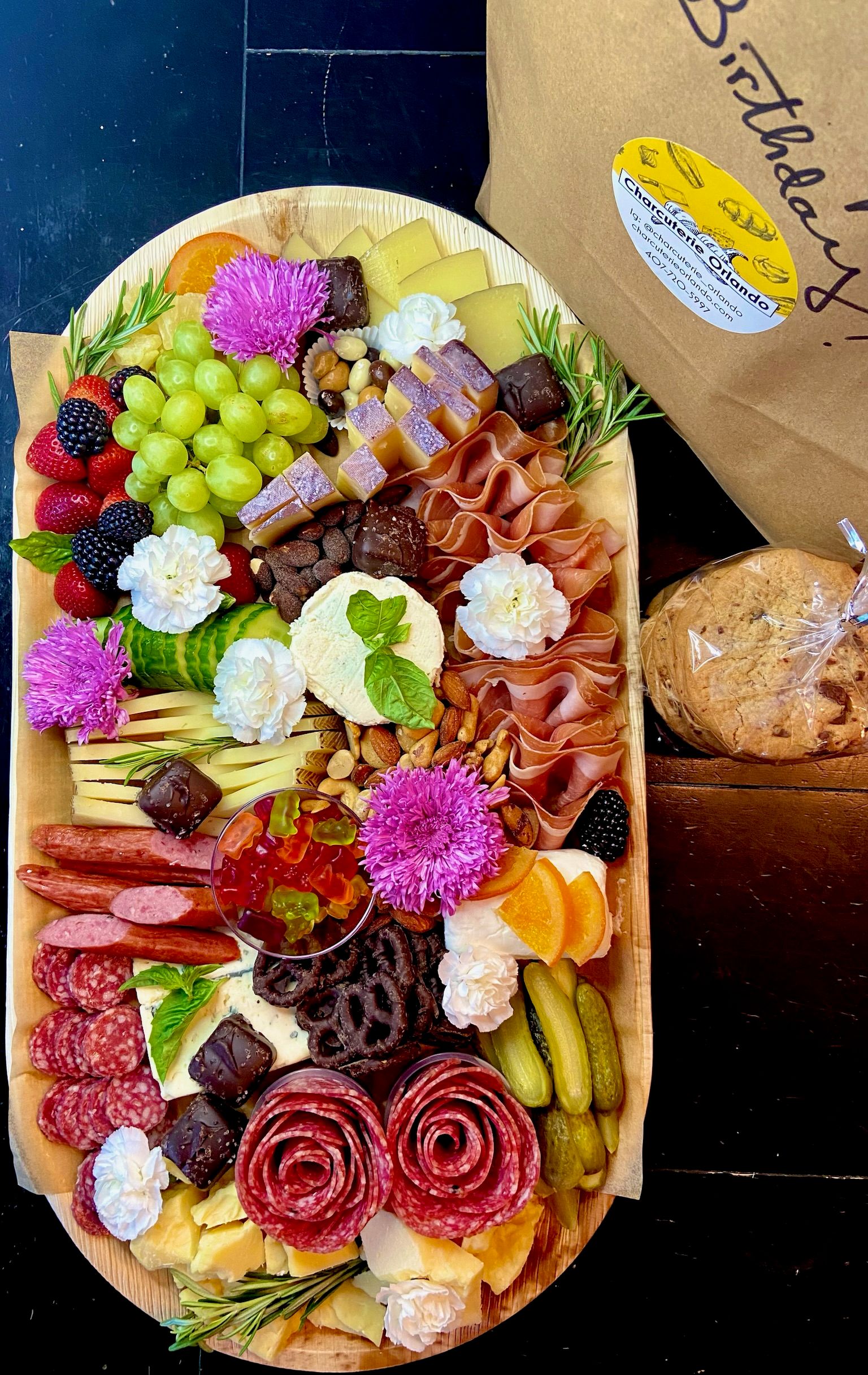 A large platter filled with meats , cheeses , fruits and flowers.