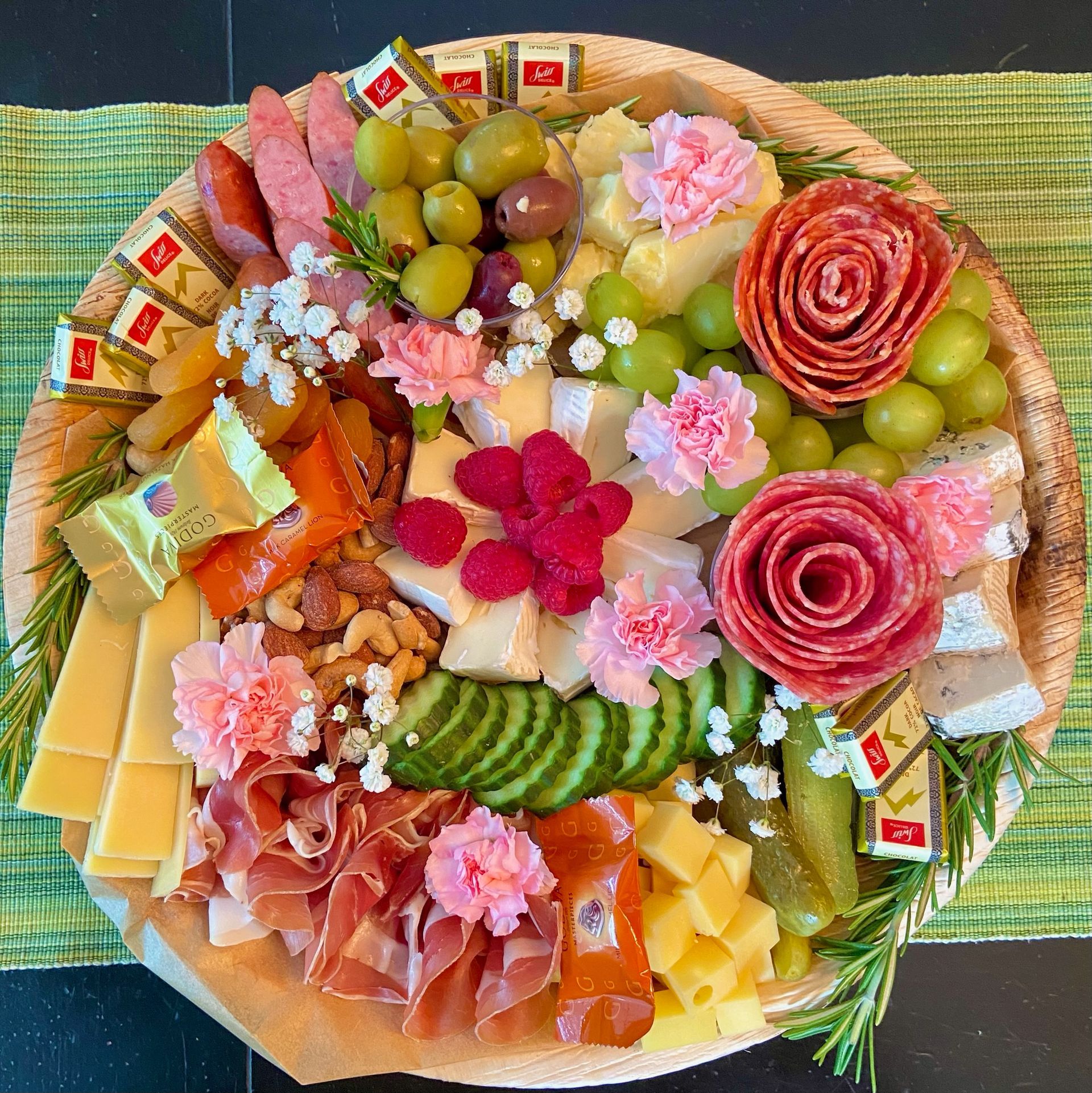 A wooden cutting board filled with meat , cheese , vegetables and flowers.