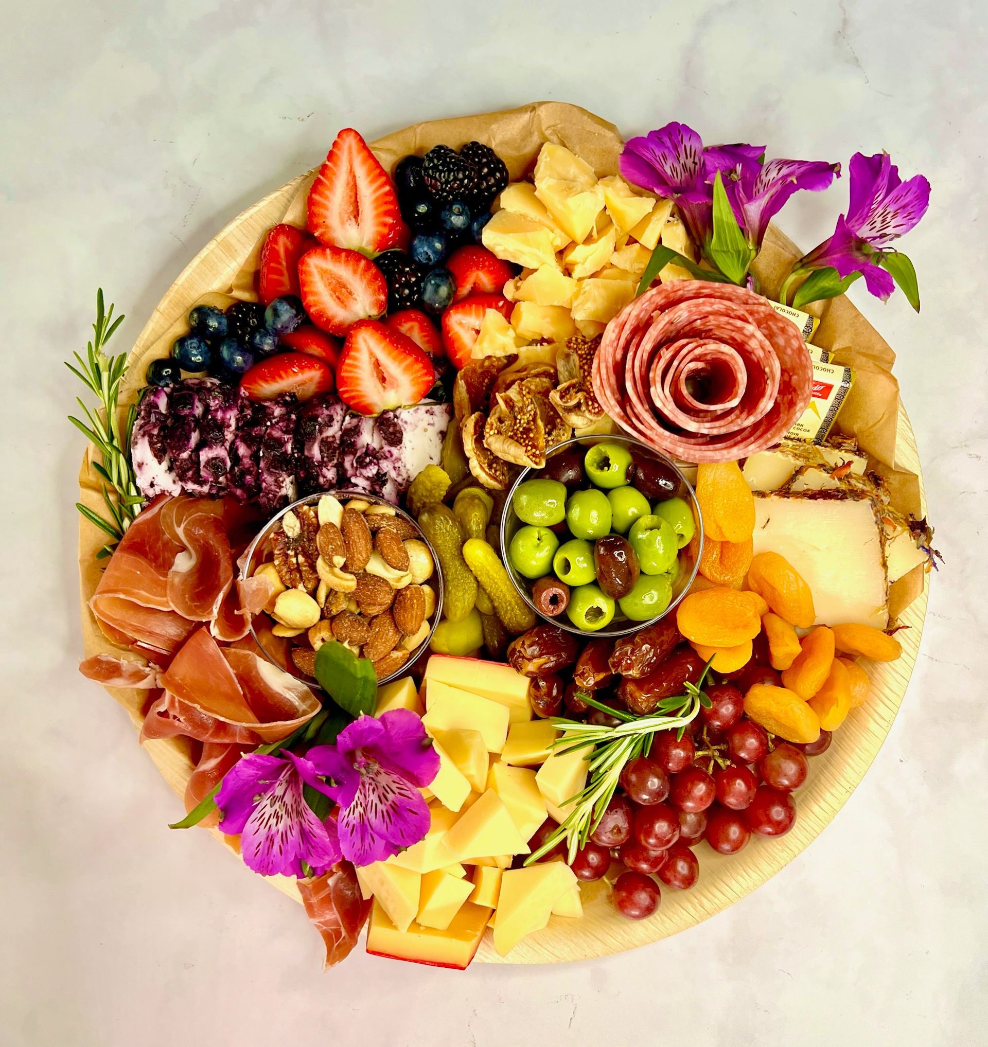 A plate of food with meat , cheese , fruit , nuts and flowers on a table.