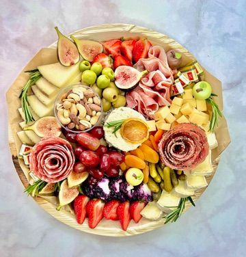 A wooden tray filled with fruits , meats , cheeses and nuts.