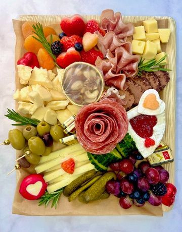 A wooden cutting board filled with meats , cheeses , fruits and vegetables.