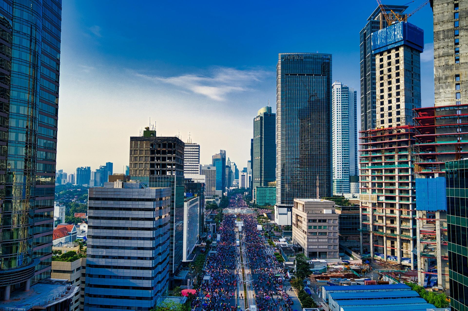 Cityscape with tall buildings, a street lined with traffic, and a blue sky overhead.