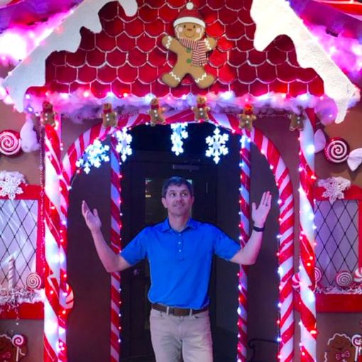 A man in a blue shirt is standing in front of a gingerbread house