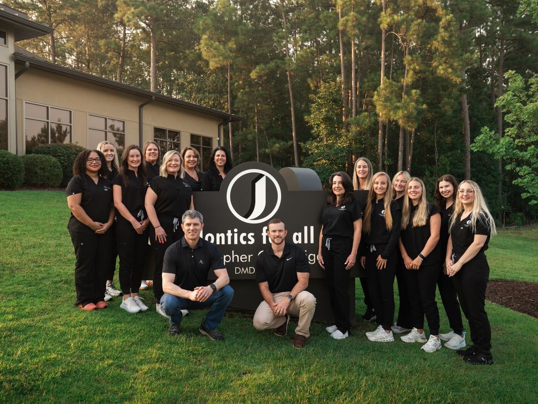 Group of people in black shirts posing outdoors beside a company sign and building.