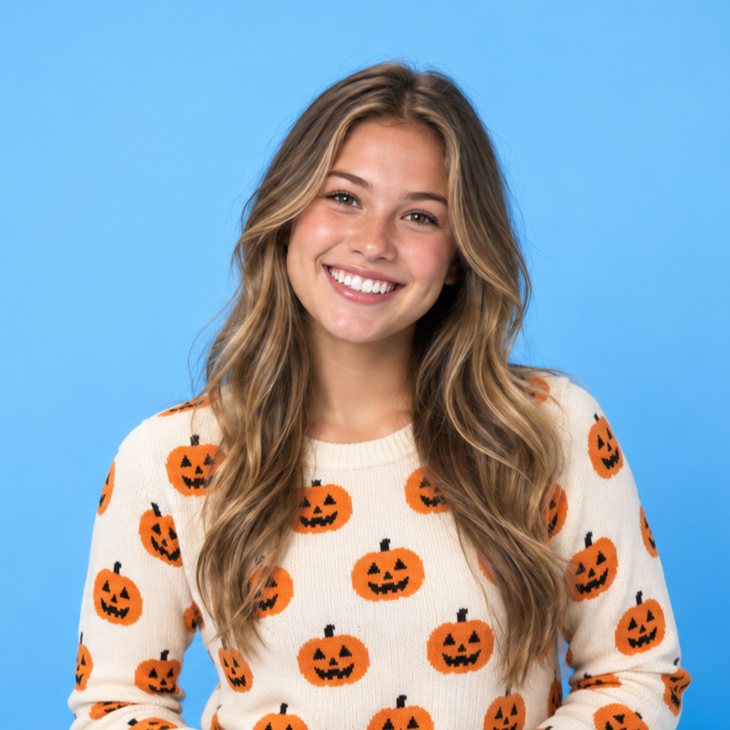 Smiling woman in a white sweater with orange jack-o'-lanterns against a blue background