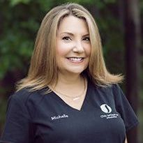 A woman in a black scrub top is smiling for the camera.