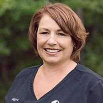 A woman in a black scrub top is smiling for the camera.