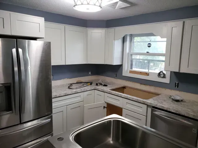 a kitchen with white cabinets , stainless steel appliances , a sink and a refrigerator