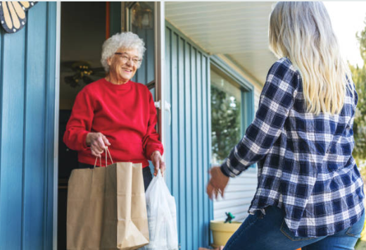 A woman is giving a bag of food to an elderly woman.