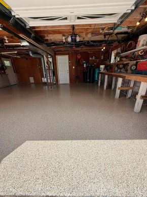 Garage interior with speckled floor, open ceiling, tools, and a white door at the back