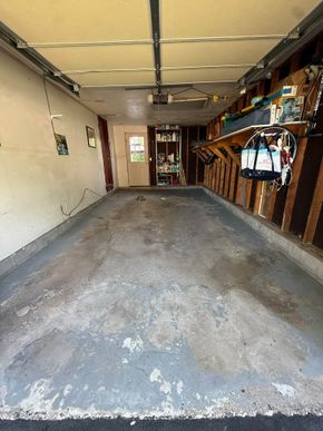 Empty garage with a concrete floor, white walls, and shelves/tools along the right side.